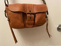 Front view of brown textured leather bag showing large buckle and two front pockets.