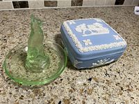 Photo showing the German Shepherd Vaseline glass ring holder next to the blue square ceramic Wedgwood trinket box with white classical reliefs on the lid and floral sides.