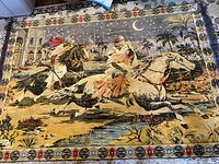 Full photo of vintage velvet tapestry depicting two men on horses and a bride, detailed background with palm trees, palace, crescent moon, and decorative border with tassels