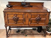 Front view of English Jacobean style buffet showing rectangular raised tabletop with gadrooned edge and backsplash, two wood panel doors with carved octagonal medallions, barley twist legs with H stretcher base.