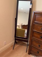 Full view of the cheval standing mirror angled and resting against a wall, showing its support legs and frame.