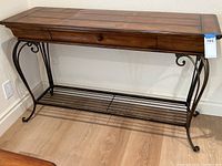 Full view of console table showing wood top, single drawer with wooden knob, and metal ornamental scrollwork base with lower slatted shelf.