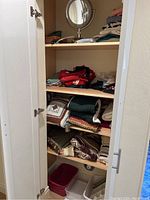 View of the contents inside the closet showing folded blankets, pillows, and storage boxes on shelves and floor.