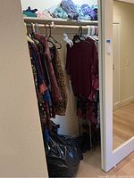 Photo of double closet with hanging womens clothing items and various colors and prints visible, black bag on floor