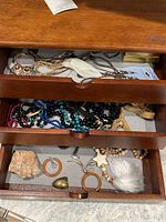 Top view of the three wooden drawers filled with assorted costume jewelry including beaded necklaces, feather brooches, gold-tone pieces, and earrings.
