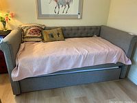 Front view of grey upholstered daybed with pink quilt and decorative pillows