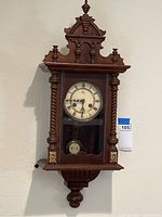 Front view of wall clock showing wood case, porcelain dial, twisted columns and pendulum visible through glass door