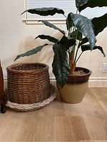 Faux potted plant with large dark green leaves and two wicker baskets side by side on floor against wall.