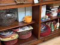 Four shelves holding stacked colorful salad plates and bowls, with a large clear glass bowl and a yellow ceramic mug on center shelf.