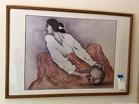 Wide view of framed art print showing Native American woman seated on rocks holding pottery vessel.