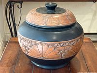 Front view of the large ceramic pot with lid, showing geometric terracotta sunburst and star patterns on black ceramic body.