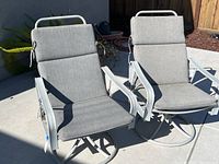 Two aluminum swivel patio chairs with gray cushions on a concrete surface outside, showing overall view of both chairs.
