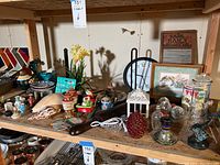Wide view of shelf loaded with assorted collectible and decorative items including vases, figurines, clock, framed art, and other knick knacks.