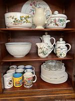 Three shelves showing assorted dinnerware and mugs with floral designs and some glass dishes