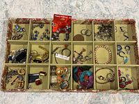 Overview of full tray showing multiple compartments filled with various earrings, bracelets, and pendants