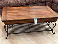 Front view of the wood top and metal base coffee table showing wood grain, drawer front and metal slatted bottom shelf.