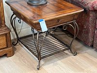 Square side table showing wood top, metal base with decorative curved legs and lower metal slatted shelf