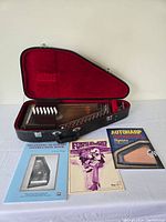 Open hard shell case with autoharp inside and three booklets arranged in front
