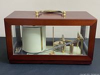 Front view of wood and glass case showing brass handle and interior mechanism with paper chart drum.