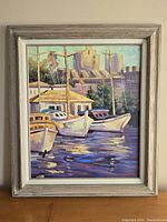 Full view of framed oil painting showing three sailboats docked in water with buildings in background