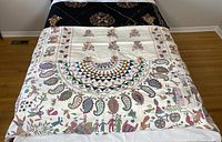 White embroidered bed cover draped over bed with black quilted cover at headboard