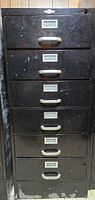 Front view of black metal filing cabinet showing six drawers with silver label holders and handles