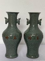 Pair of celadon vases with crackle glaze and two animal-like handles on neck, brown characters around body.