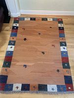 Full view of the Gabbeh area rug on wooden floor, showing center field, colorful border and fringe.