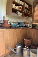 Corner cabinet and countertop displaying various pots and the terra cotta plant stand with two metal watering cans