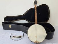Photo showing full vintage banjo resting on an open black hard case, with harmonica and neck holder placed in front.