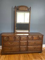 Full frontal view of the wooden dresser with nine drawers and matching framed mirror above it.