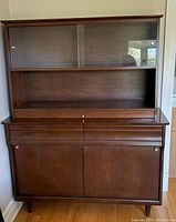 Front view of walnut Krug hutch/display cabinet showing upper glass sliding doors, open middle shelf, drawers and lower sliding-door storage