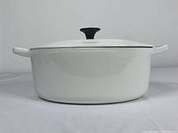 Front view of oval Dutch oven with lid closed showing white enamel finish, black knob, and side handles.
