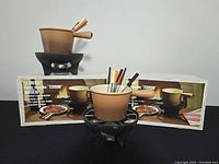 Two Le Creuset fondue sets displayed on black surface with original boxes in background
