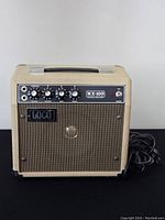 Front view of Loco MX-100 musical amplifier showing control panel with four knobs and power switch, cream casing, and speaker grille with LOCO branding.