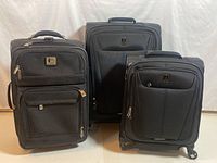 Front view of three black suitcases including Kenneth Cole Reaction carry-on on left and two Tracelpro suitcases of varying sizes on right