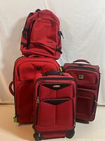 Four red luggage pieces including backpacks and suitcases displayed against white background
