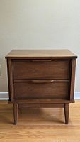 Front view of the walnut bedside table showing two drawers and tapered legs
