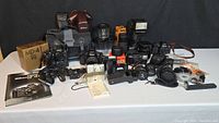 Wide view of entire lot on white table showing two camera bodies, lenses, bag, flash and accessories.