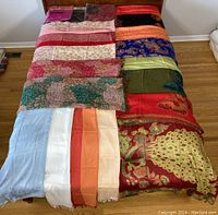 Full view of all scarves and pashminas laid out on bed, showing range of colors and patterns.