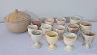 Wide view showing the covered bowl and fourteen soapstone goblets arranged in rows on a flat surface, showcasing natural soapstone color variations and veining.