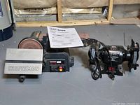 Photo showing the Craftsman belt/disc sander and JobMate bench grinder side by side on a gray floor.