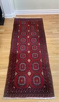 Full length view of the wool runner on a hardwood floor, showing the repeating geometric medallion pattern in red, cream, black, and brown.