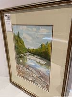 Framed signed watercolor landscape artwork showing river, trees, sky, 17x21.5 inches, front view.