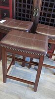 Three brown faux leather cushioned bar stools with wooden legs and brass nailhead trim, shown from side angle
