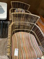 Photo showing two cane and wicker chairs with armrests and seat cushions in striped and floral patterns.