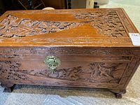Front view of carved wooden chest showing detailed carvings and brass-tone clasp lock.