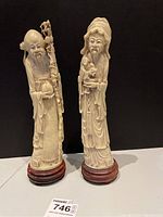 Two full-height carved figures on wooden bases against black background