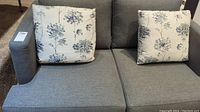 Front view of grey loveseat with two floral throw pillows