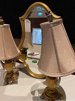 Two beige-shaded table lamps with amber-toned bases and a gold-framed mirror with curved top reflected in the background.
